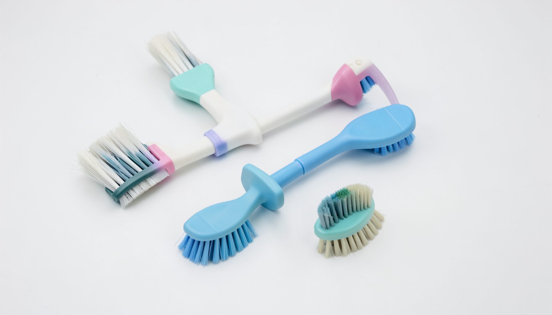 Four small colorful cleaning brushes with pastel blue, pink, teal and white handles scattered on a white surface