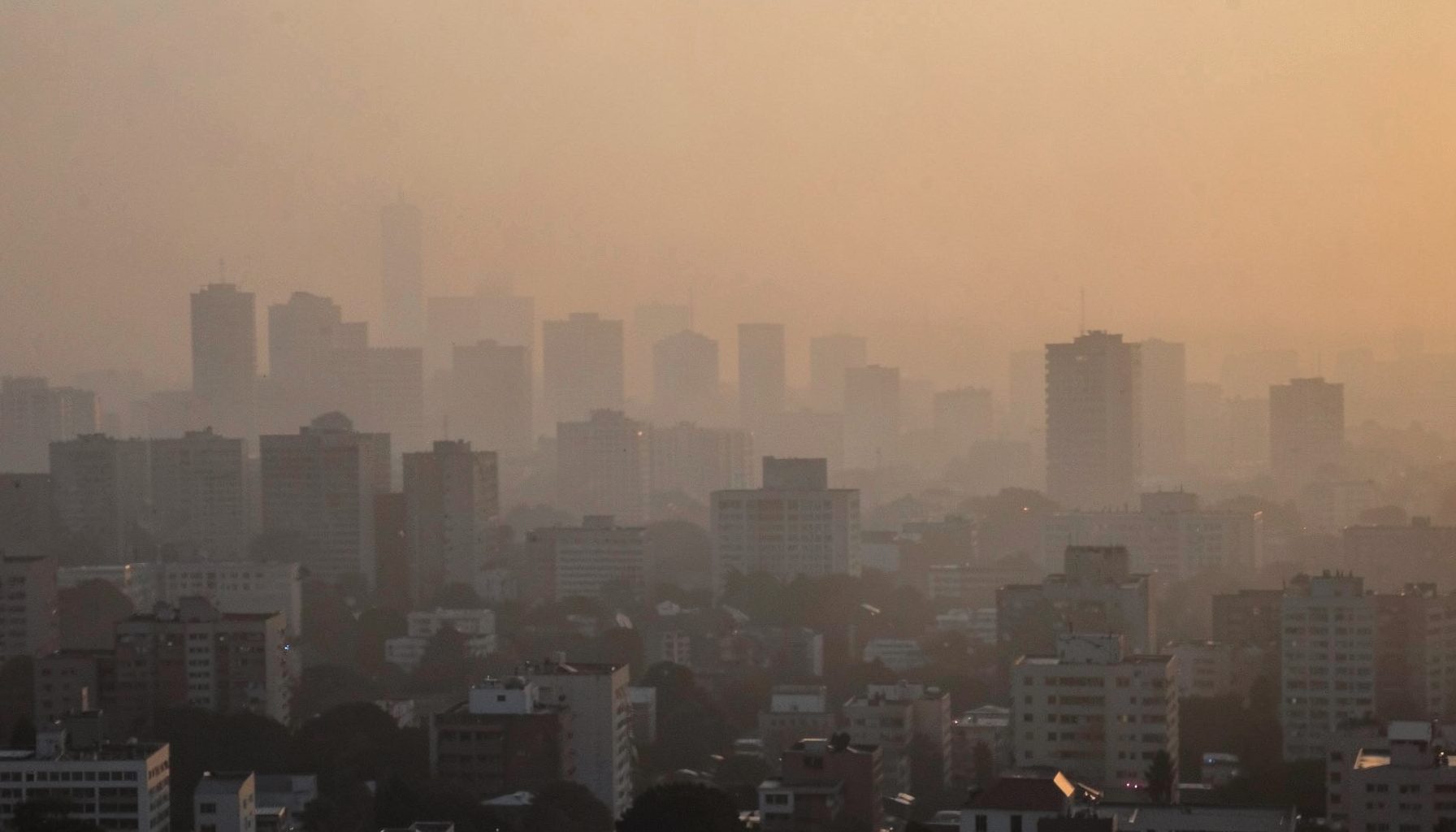 Hazy city skyline at dusk with muted orange-gray tones, suggesting air pollution and urban living